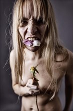 Young naked woman eating the petals of a rose and looking aggressively into the camera