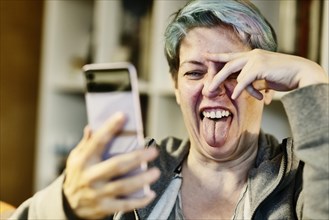Woman with dyed hair sticks out her tongue at her smartphone