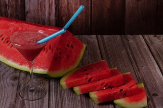 Cocktail glass with watermelon juice and slices of fresh watermelon on a wooden table
