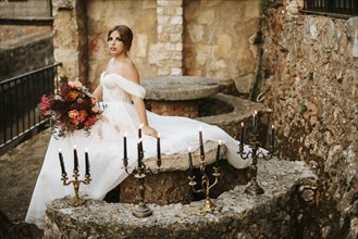 Beautiful bride with her bouquet sittitng in the stone garden with candles