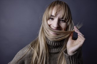 Young woman with long blond hair smiling and holding a strand of hair in front of her mouth