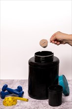 Woman pouring a scoop of protein powder in an insulated shaker on a black background