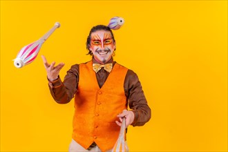 Juggler in a vest with makeup juggling with maces on a yellow background