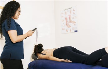 Professional physiotherapist electrostimulating a lying patient