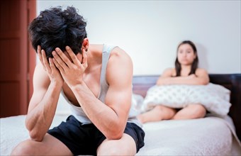 Worried man sitting on the side of the bed and angry wife
