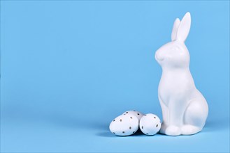 Easter bunny and white and gold Easter eggs with dots on blue background with copy space