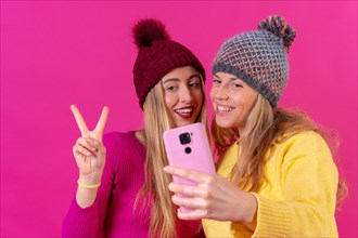 Two young blonde caucasian women with a phone isolated on a pink background