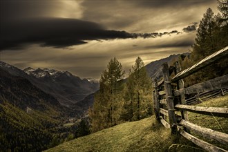 Wooden fence with autumnal mountain forest and threatening cloudy sky