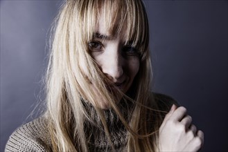 Young woman with long blond hair covers one half of her face with a strand of hair and looks saucily into camera