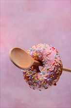 Donut on wooden spoon against pink background