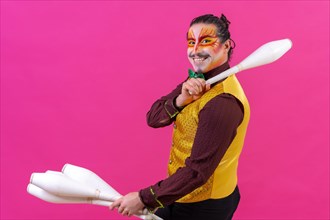 Portrait of a juggler in a waistcoat and with painted face juggling maces on a pink background