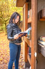 Attractive woman looking into books next to bookshelf in forest