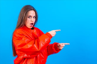 Attractive woman smiling pointing fingers at copy space on blue background