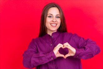 Young brunette woman wearing purple sweater over isolated red background smiling in love making heart symbol shape with hands. romantic concept