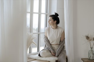 Dark-haired woman sits relaxed at the window