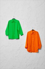 Two bright green and orange shirts on hanger hang on white wall
