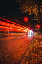 Long exposure of moving cars on a road just in front of an intersection with traffic lights at night with lanterns lit