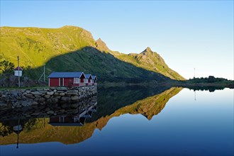 Wooden houses and mountains reflected in the shallow fjord water