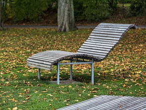 Empty wooden sun lounger in a meadow with autumn leaves