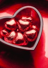 Small red chocolate hearts in heart-shaped glass bowl