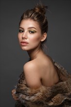 Portrait of a beautiful woman in a furcoat with creative gold makeup in a fashion style. Beauty face. The photo was taken in a studio on a black background