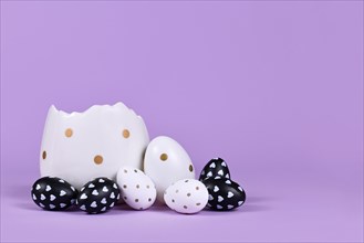 Black and white easter eggs with dots and hearts and egg cup on violet background
