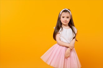 Cute little girl stands in a yellow-tinted studio