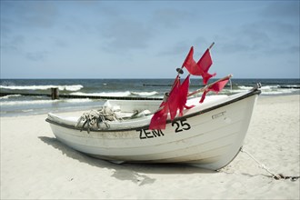 A small white fishing boat lies on the beach. Red flags and ropes lie in the boat. In the background you can see the sea