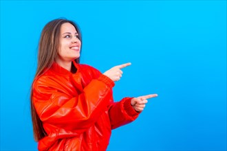 Attractive woman smiling pointing fingers at copy space on blue background
