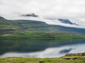 Fog drifts over lonely hills by a fjord