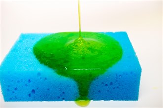 Green liquid soap dripping on a blue sponge on a white background