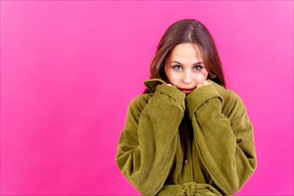 Beautiful young woman wearing warm green woolen sweater on pink background. space for text