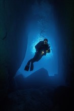 Diver with underwater lamp shines swims in cave underwater underwater cave in background light daylight light incidence through cave entrance