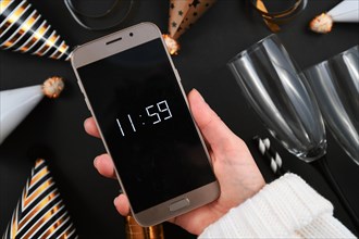 New Year Silvester celebration concept with hand holding smart phone with timer countdown to midnight in front of champagne drinking glasses