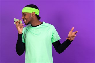 Black ethnic man with a phone in green clothes isolated over purple background