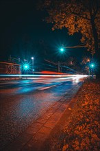 Long exposure of moving cars on a road just in front of an intersection with traffic lights at night with lanterns lit