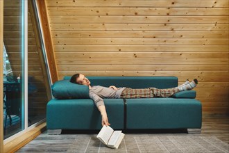 Man was reading a book in his wooden cabin in rainy day and fell asleep