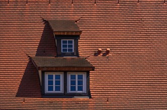 Three dormers with mansard windows in a roof structure covered with red tiles