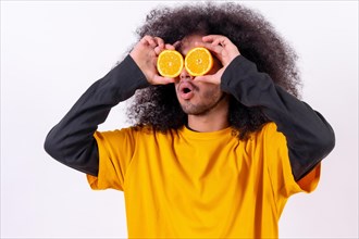 Portrait with the orange fruit in the eyes split in half. Young man with afro hair on white background