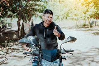 Biker on his motorbike holding safety helmet with thumb up. Concept of Smiling motorcycle cyclist holding safety helmet