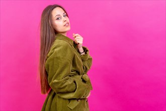 Close up portrait of young caucasian woman in green trench coat isolated on pink background