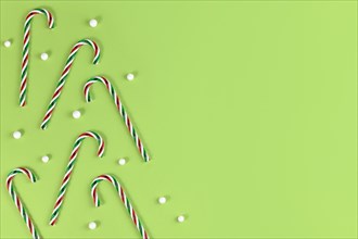Striped candy cane Christmas sweets with snowballs on side of green background with copy space