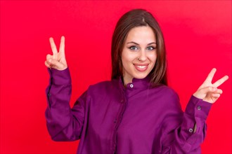 Young woman isolated on red background smiling and showing victory sign wearing red shirt