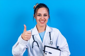 Portrait of smiling female doctor in medical gown standing isolated on blue