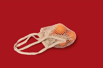 Oranges in a string bag on ruby red background. Concept of sustainable living