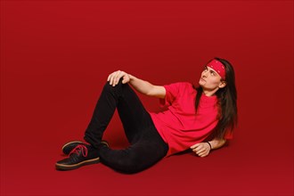 Active young man with long hair and head band sitting on floor in red studio