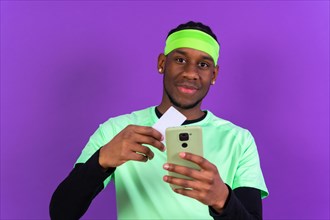 Black ethnic man with a phone in green clothes on a pink background