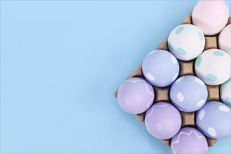 Box of pastel colored easter eggs on blue background with copy space