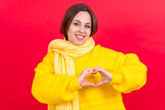 Young brunette woman wearing yellow sweater over isolated red background smiling in love making heart symbol shape with hands. romantic concept