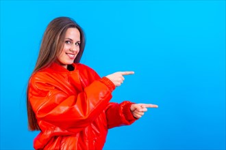 Attractive woman smiling pointing fingers at copy space on blue background